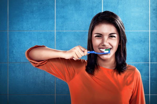 A Lady brushing teeth in front of tiles