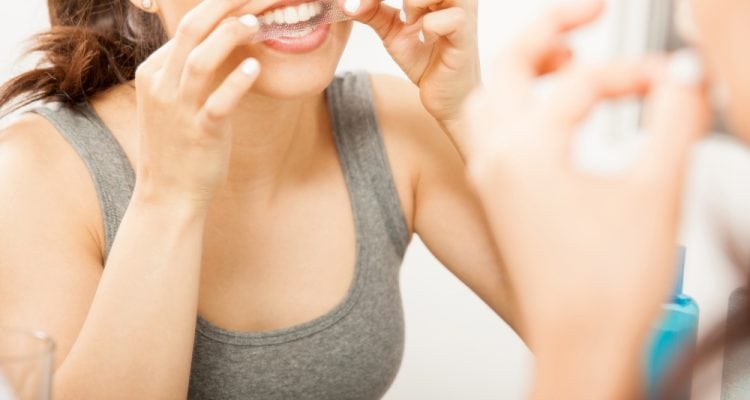 Close up of woman putting whitening strip on her teeth
