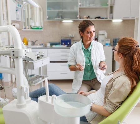 Female dentist in dental office talking with female patient and preparing for treatment