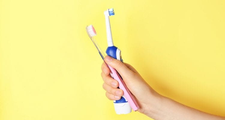 Woman holding manual and electric toothbrushes against colour background