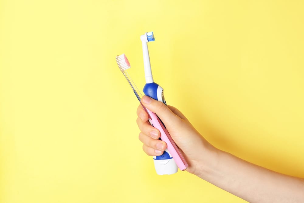 Woman holding manual and electric toothbrushes against colour background