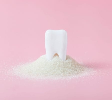 Plastic tooth in big pile of sugar. Caries and sugar concept. Dental care concept on pink background