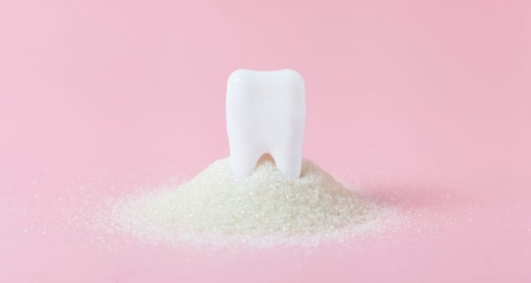 Plastic tooth in big pile of sugar. Caries and sugar concept. Dental care concept on pink background