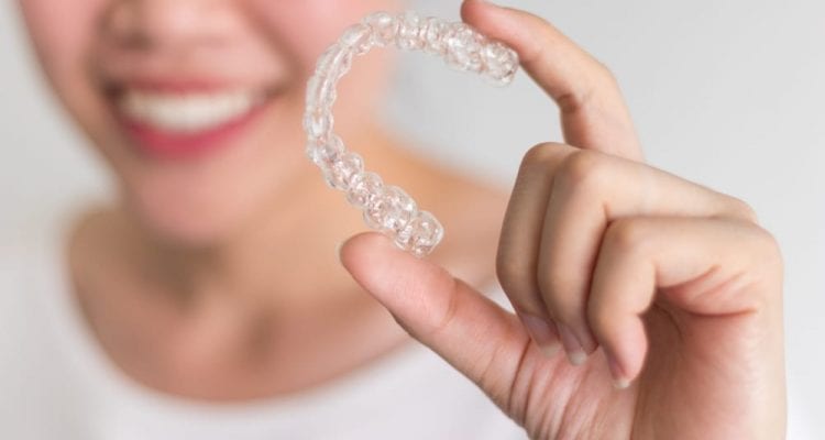A smiling woman holding Invisalign or invisible braces.