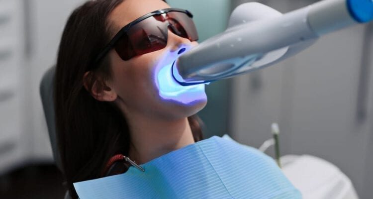 Female patient at dentist in the clinic. Teeth whitening procedure with ultraviolet light UV lamp.